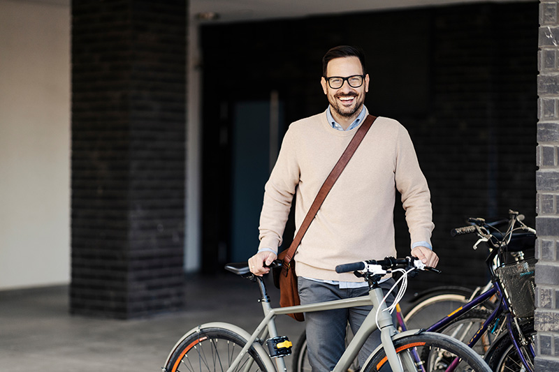 A smiling man stands outdoors and holding bicycle.