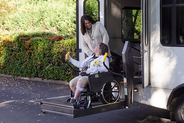 A woman in a wheelchair is helped off a van using a chair lift.