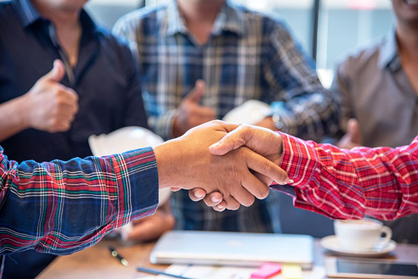 Two people shaking hands and people in the back with thumbs up