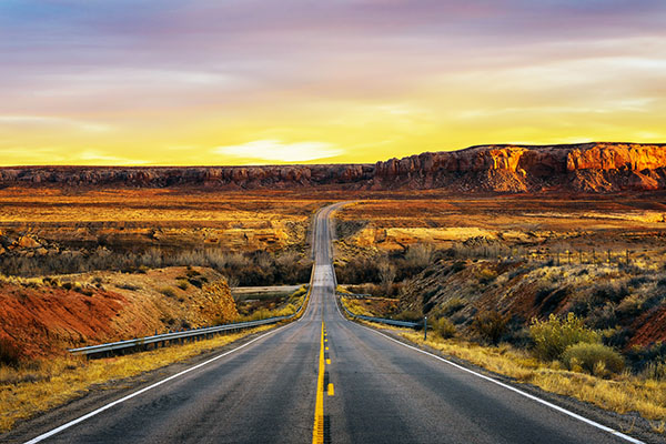 A long road with southern Utah mountains in the distance