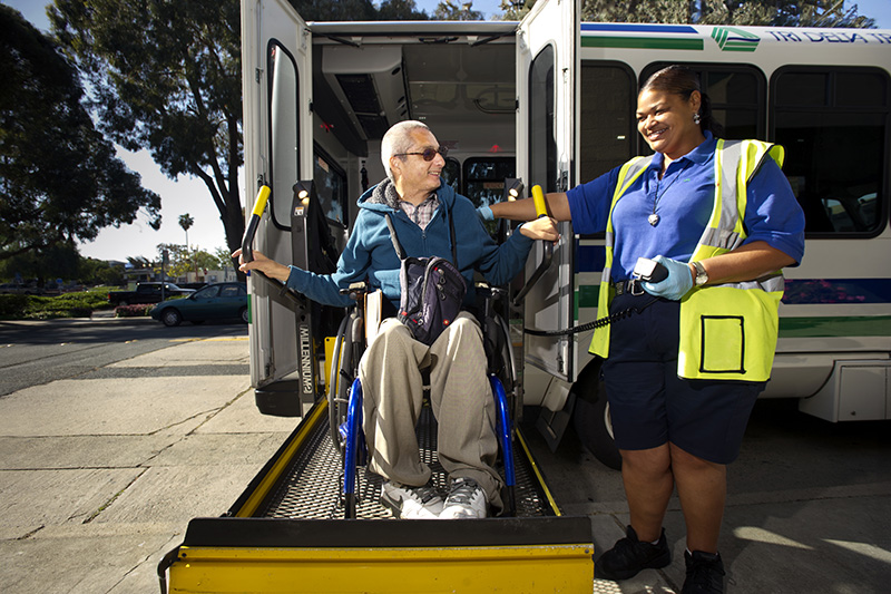 A bus operator helping a gentleman use the wheelchair lift and smiling